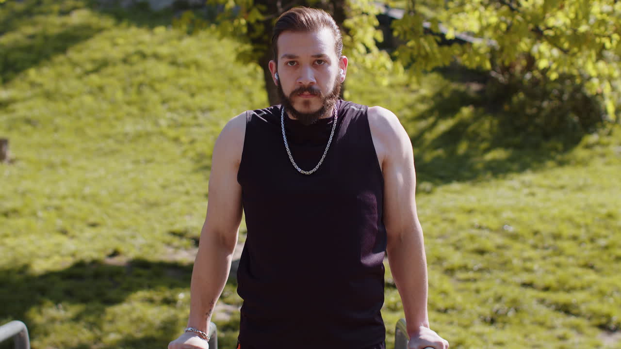 Athletic lebanese man in sportswear practicing dips on parallel bars training triceps on playground