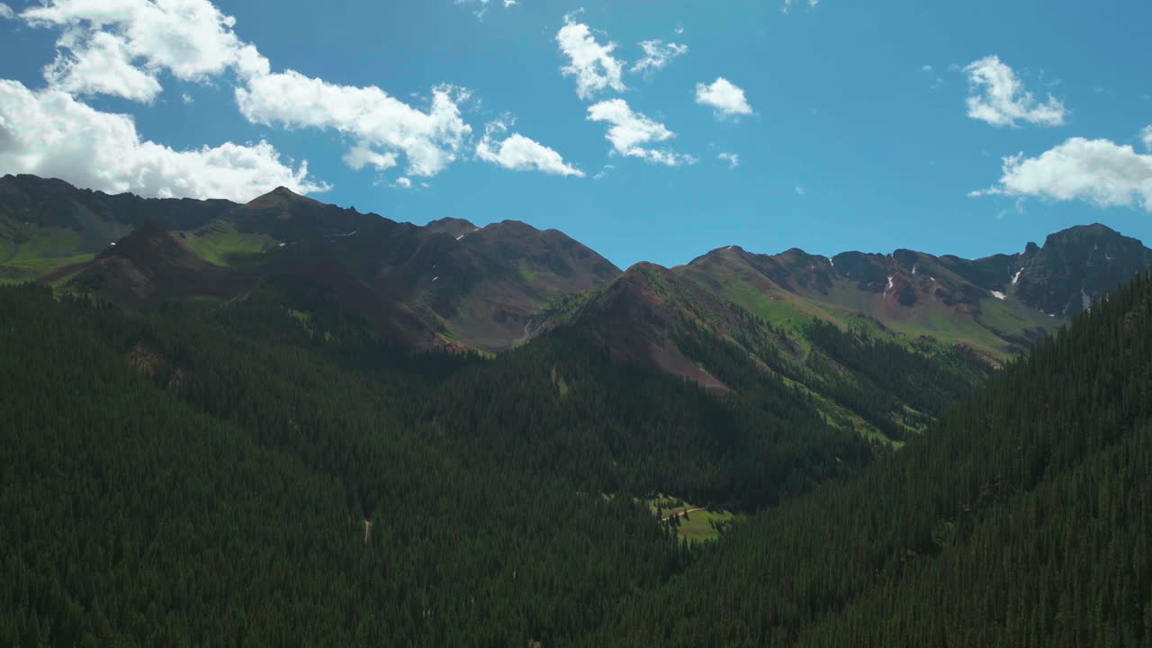Aerial cinematic drone summer high altitude Silverton Mountain Ski Resort southern Colorado blue sky late morning stunning lush green blue sky partly cloudy Rocky Mountains upward jib motion