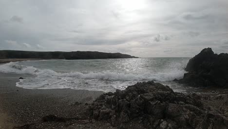 Cámara-Lenta-Tranquilas-Olas-Espumosas-Del-Océano-Chocando-Contra-La-Rocosa-Costa-Arenosa-Galesa-Al-Amanecer