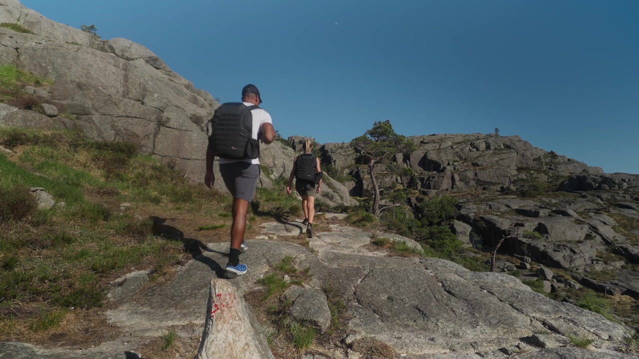 Escursionisti camminano attraverso grandi massi di granito in un drammatico paesaggio di fiordi norvegesi con un terreno roccioso simile alla luna sotto un cielo azzurro e limpido