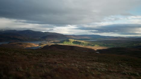 shafts of light burst through dark clouds to highlight splashed of green and orange in a scottish landscape of mountains and lochs