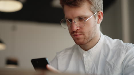 adult european man with glasses is using modern mobile gadget surfing internet by smartphone portrait shot