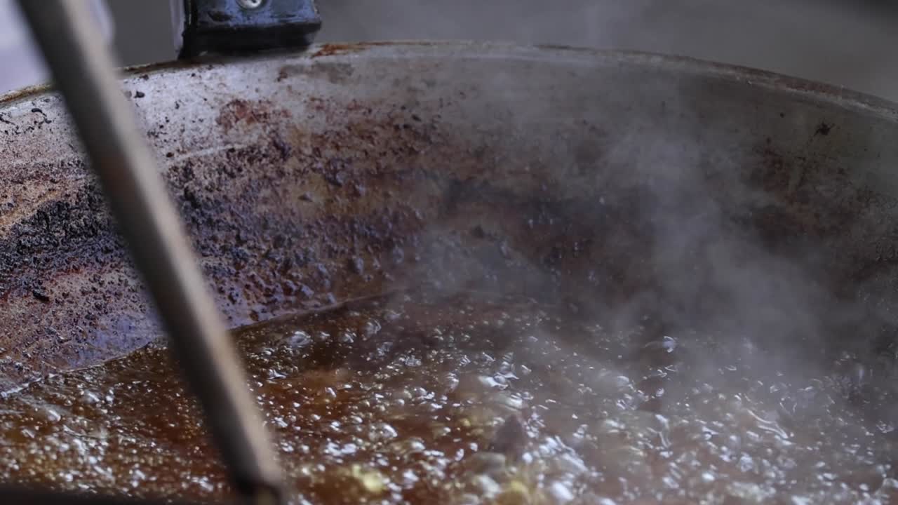 Extreme close-up of meat frying in bubbling oil with steam rising from a metal wok