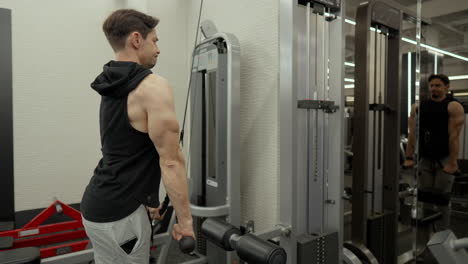 man doing cable rope tricep extension exercise and looking ar mirror reflection - side view