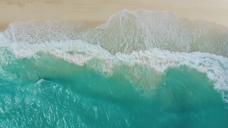 top down birds eye view of waves crashing on tropical white sand beach