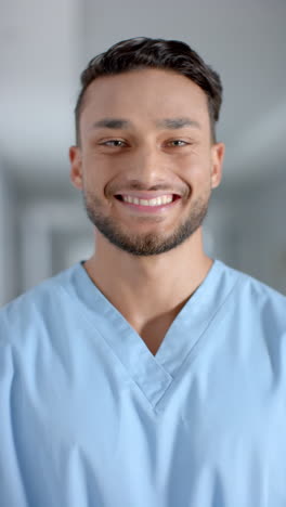 vertical video of portrait of happy latino male doctor wearing scrubs, slow motion