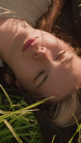 mujer acostada pacíficamente en una tela extendida sobre un campo de hierba, rodeada de altas hojas verdes de hierba y la cálida luz del sol proyectando sombras suaves en su rostro
