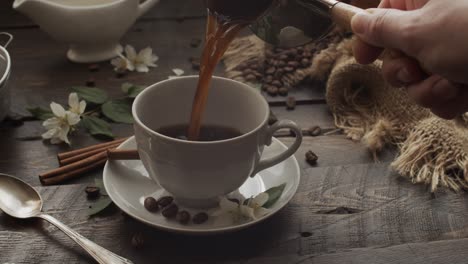 Filling Cup with Freshly Brewed Turkish Coffee from Cezve on Wooden Table