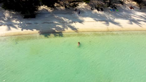 An-aerial-drone-pedestal-up-shot-tilting-slowly-from-the-beachfront-of-Shark-Bay-revealing-the-seashore-with-some-tourists-sunbathing-and-swimming-in-its-shallow-waters,-in-Koh-Tao-island,-Thailand