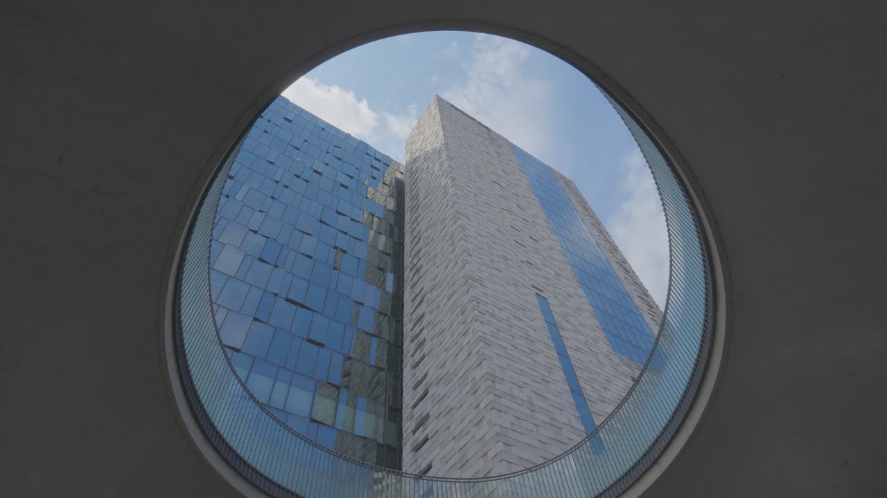 A unique low-angle view of the Shinjuku Eastside Square skyscraper, framed through a circular window or architectural element