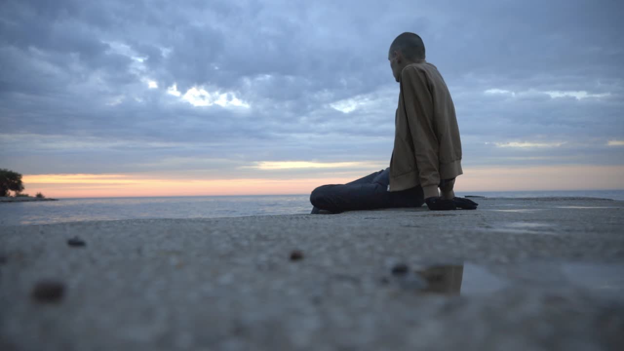 아름다운 자연을 보면서 해안에 앉아 있는 젊은 남자의 낮은 각도 - 와이드 샷