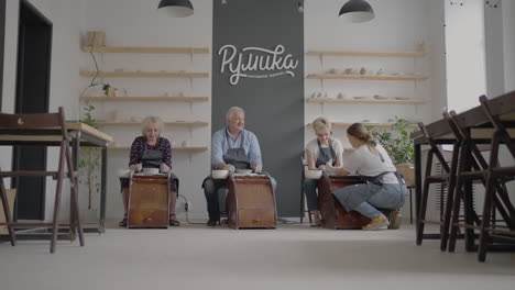 disparo medio de un artista de cerámica de mediana edad que enseña a un grupo de ancianos, una mujer caucásica y un hombre mayor cómo hacer arcilla sentados en un escritorio en un estudio de arte. personas que disfrutan hablando en el trabajo