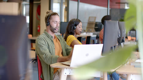 Hombre-De-Negocios-Casual-Caucásico-Y-Colegas-Diversos-Usando-Auriculares-Telefónicos-Y-Computadoras,-Cámara-Lenta