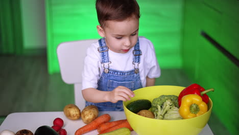 child exploring vegetables indoors. a young boy sits at a table in a bright kitchen, curiously examining fresh potatoes and carrots