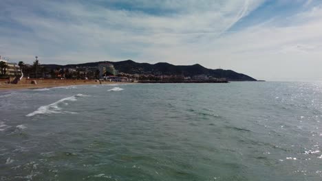 vista panorámica de la costa de sitges con olas suaves, un mar tranquilo y montañas en el fondo