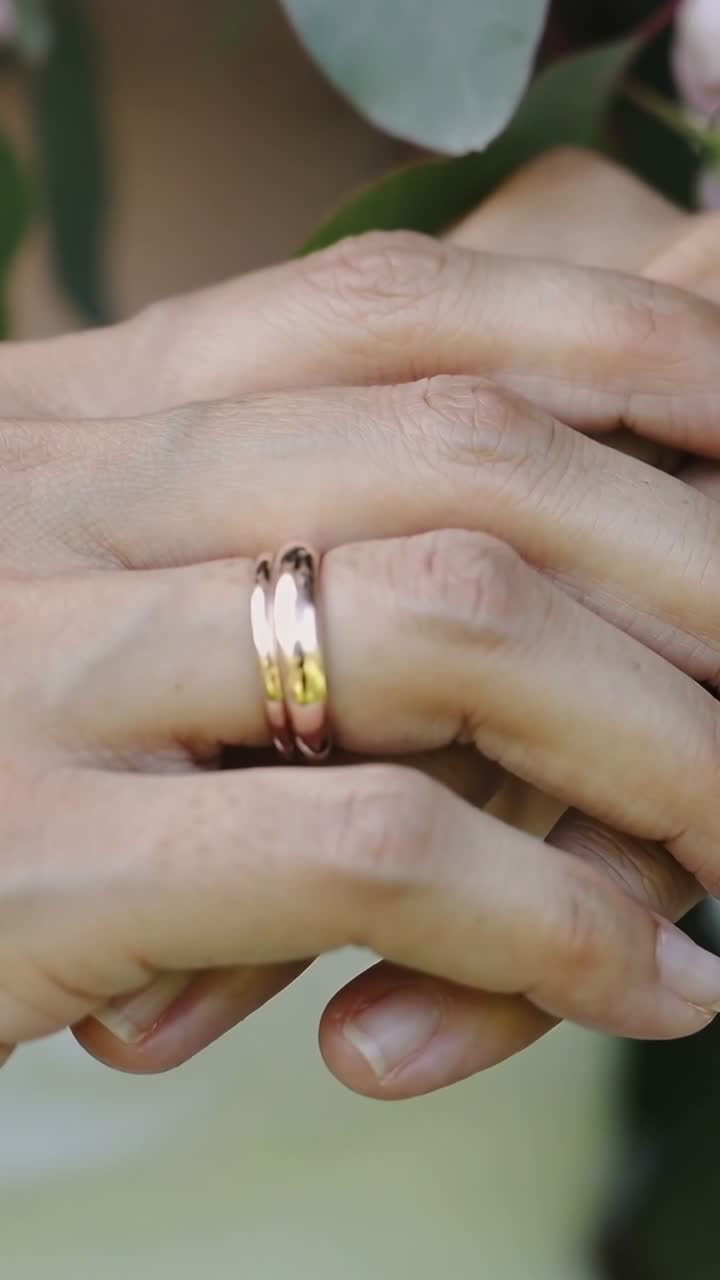 Video verticale: Inquadrature che mostrano mani che si muovono in un bouquet, primo piano di anelli a due fasce e con gemme che brillano.