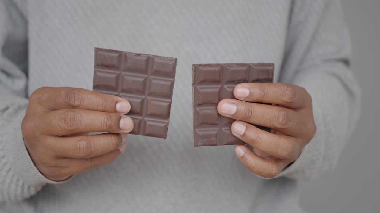 Hands holding two pieces of a broken chocolate bar
