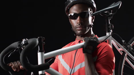 focused african american cyclist holding a bicycle on a black background