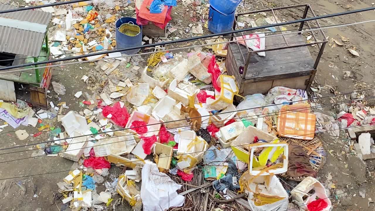 garbage and plastic debris beside slum buildings, highlighting urban pollution and sanitation problems in Bangladesh