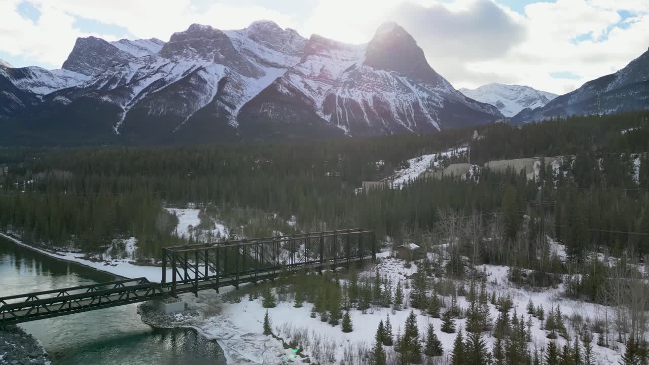 ascenso aéreo del puente de tren fluvial con montañas en el fondo, alberta, canadá