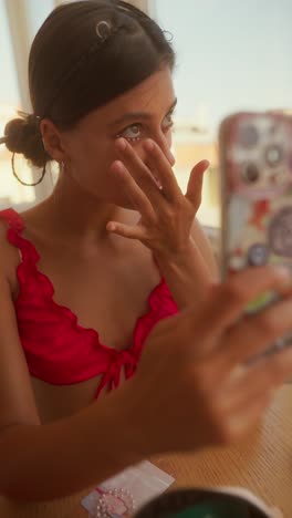 young woman applying under-eye gems while looking at phone