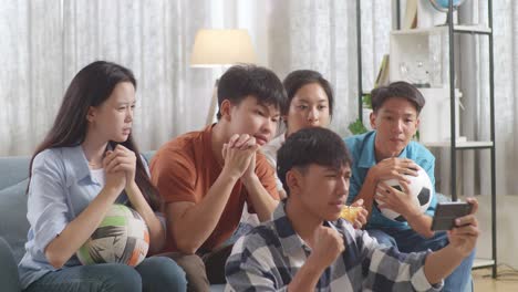 asian teenagers cheering and watching football game on smart phone and disappointed at home