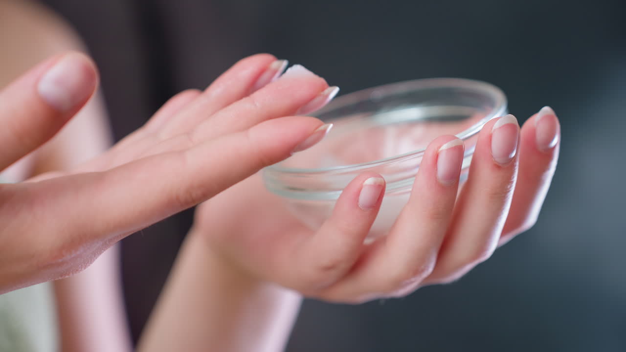 Closeup view of woman's hand gently tapping finger into transparent skincare container, preparing to apply cream as part of moisturizing beauty routine, personal care, hydration