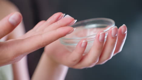 closeup view of woman's hand gently tapping finger into transparent skincare container, preparing to apply cream as part of moisturizing beauty routine, personal care, hydration