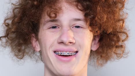 closeup of the face of a satisfied crazy happy young guy with braces closeup of the face of a satisfied crazy happy young guy with braces positive curly redhaired student on a light blue background