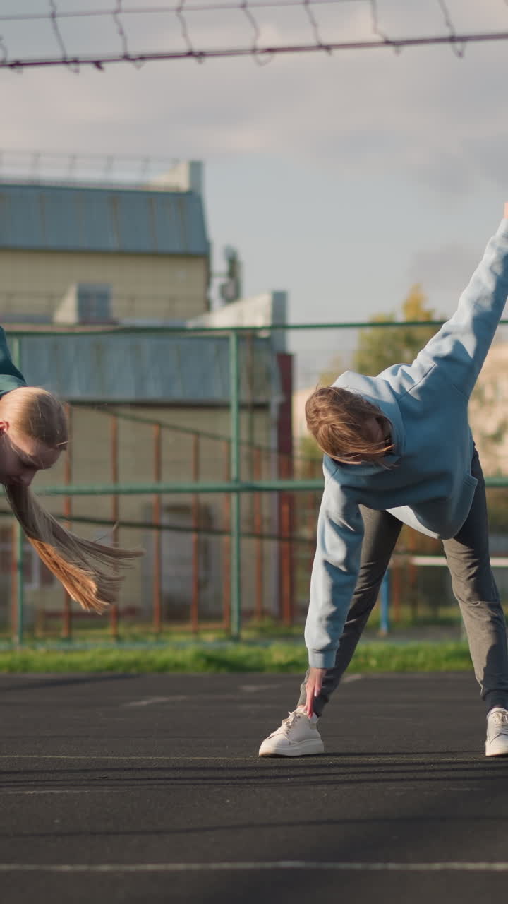 atletas realizando ejercicios de fitness en una cancha al aire libre, doblando sus cabellos en cascada hacia abajo, el fondo presenta un edificio y vegetación