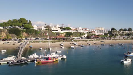 dolly aéreo lateralmente a lo largo de la costa de alvor, barcos de vela junto al muelle y la playa, algarve