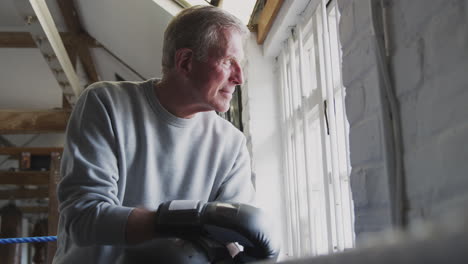 portrait of senior male boxing coach in gym standing in boxing ring