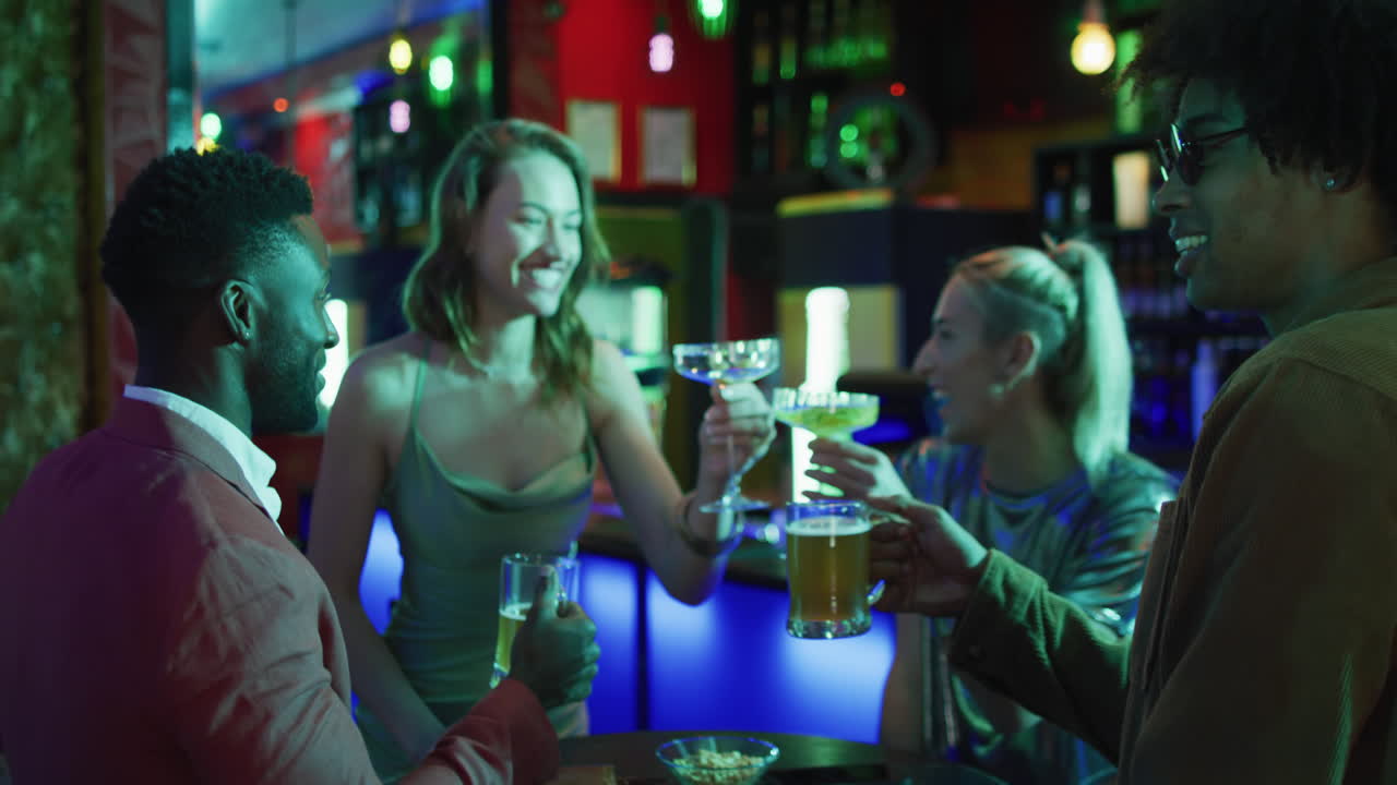 Video of diverse group of happy friends standing at a table drinking and making a toast at a bar