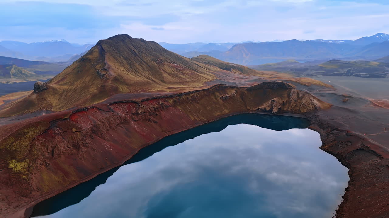 Bare mountains with no vegetation on of brown, beige and purple colors. Volcano crater is filled with water. Aerial perspective on the cosmic landscape of Iceland.