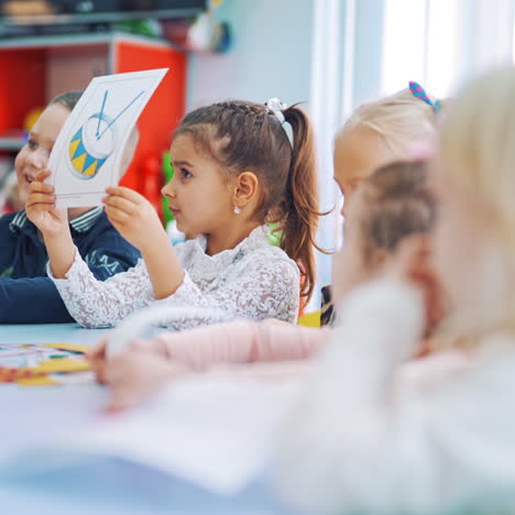 kleine jungen und mädchen lernen in der schule mit bildern. grundschüler sitzen zusammen am tisch und zeigen ihren lehrern die notwendigen bilder.