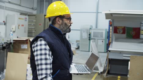 Side-view-of-serious-technician-walking-with-laptop-at-factory