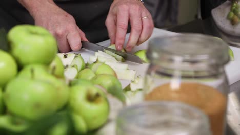 woman's hand cutting ripe green apples on chopping board by knife