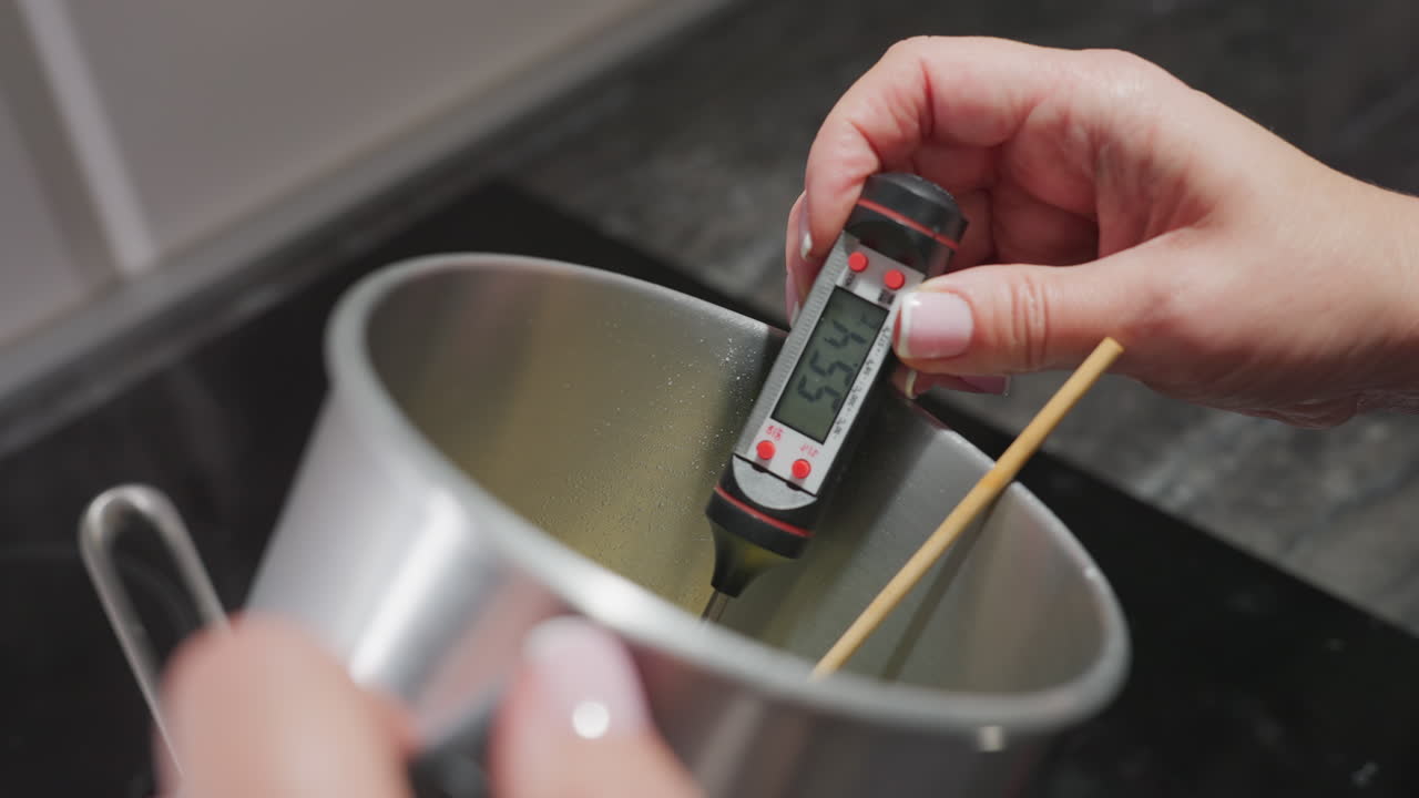 Culinary artist dips digital meat thermometer into boiling pot to measure temperature of cooking meat as reading changes from 56.9 to 55.4 degrees, showcasing precise heat monitoring in home kitchen