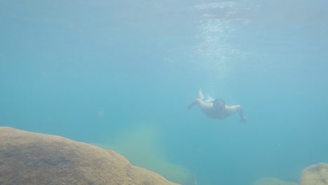 Joven-Nadando-Bajo-El-Agua-En-Agua-Azul-Clara-En-El-Día-Desde-Un-ángulo-Bajo