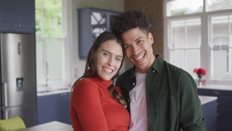 Portrait-of-happy-biracial-couple-embracing-and-smiling-in-kitchen