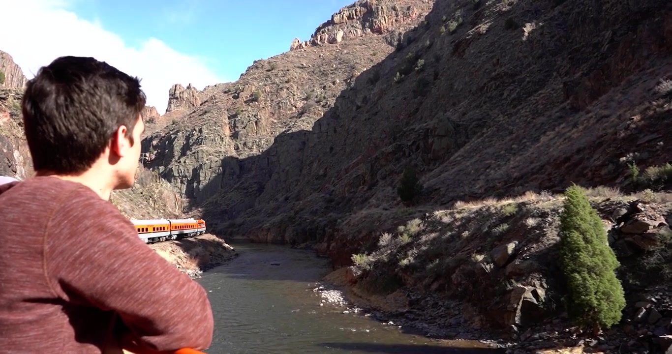 Homem admirando a paisagem de Royal Gorge, Colorado, de um vagão de observação ferroviário.