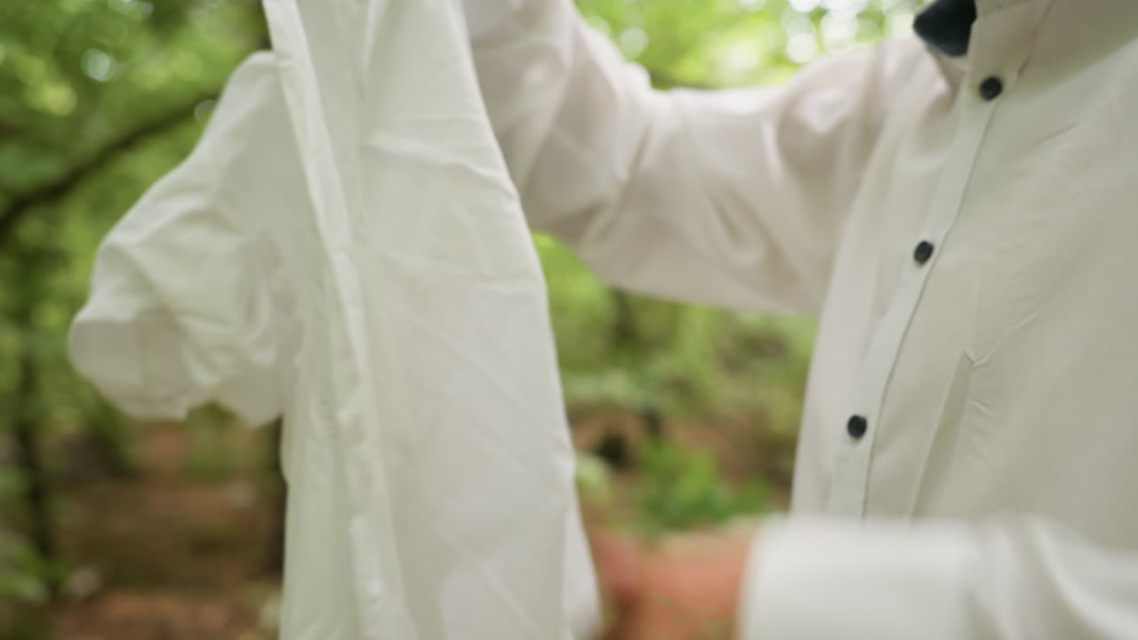 Close up view of botany student in white shirt opening coat ready to wear in forest, surrounded by natural greenery, highlighting outdoor preparation, lifestyle detail