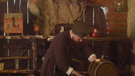 medieval keeper pours local wine from barrel at inn. barkeeper in ancient clothes fills clay mug with alcohol in tavern. concentrated servant in pub