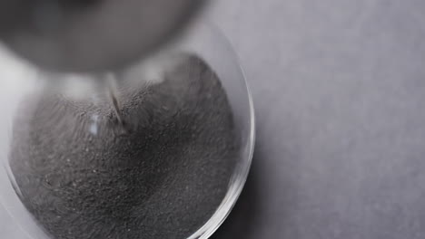 video of close up of hourglass with sand pouring, copy space on grey background