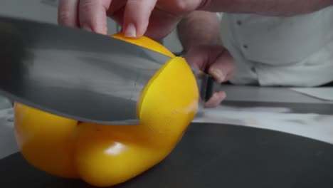 A chef is slicing a yellow pepper on a cutting board