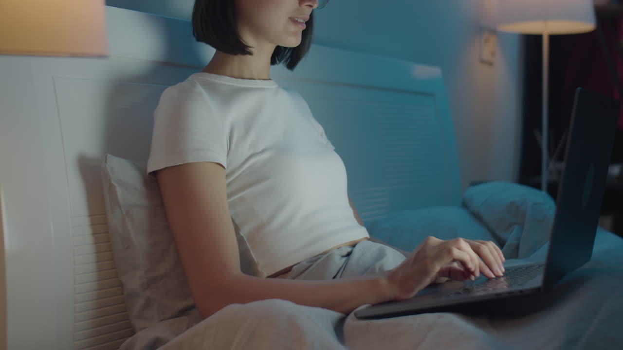 Woman Typing on Laptop on Bed in Evening