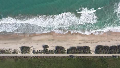 Top-shot-of-a-dirt-road-along-the-mediterranean-sea-sandy-beach-with-little-wave