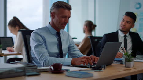 Focused-businessman-typing-on-laptop.-Male-employee-talking-with-colleague