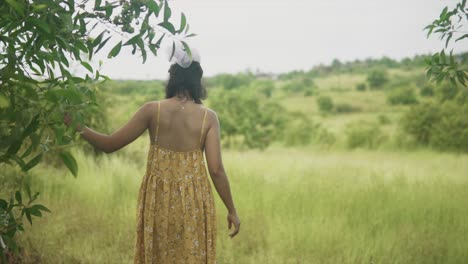 The-back-of-an-attractive-carefree-Asian-female-in-a-floral-summers-dress-exploring-alone-through-a-grass-field-and-natural-environment-on-a-beautiful-day-outdoors