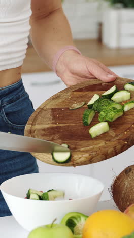 cutting a green cucumber for salad with a knife on a wooden board. vegetarian food preparation. vertical video
